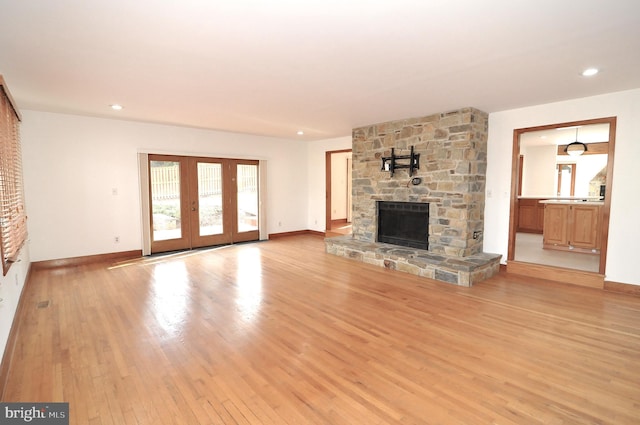 unfurnished living room with a stone fireplace, light hardwood / wood-style flooring, and french doors