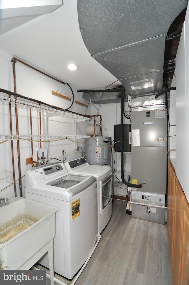 clothes washing area with sink, wood-type flooring, electric water heater, and washing machine and clothes dryer