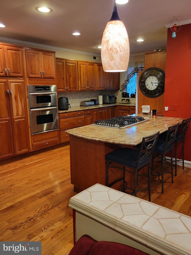 kitchen featuring a breakfast bar, backsplash, hanging light fixtures, light hardwood / wood-style flooring, and stainless steel appliances