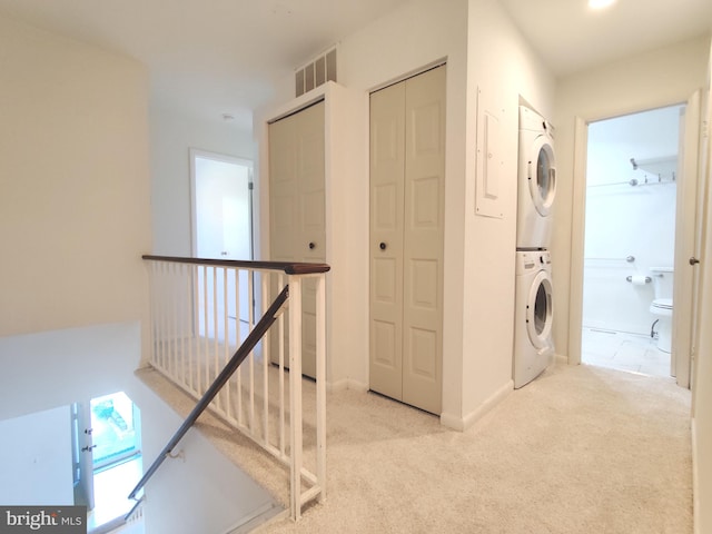 corridor featuring stacked washer / drying machine and light carpet