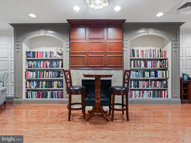 living area with a notable chandelier, light hardwood / wood-style floors, built in features, and crown molding