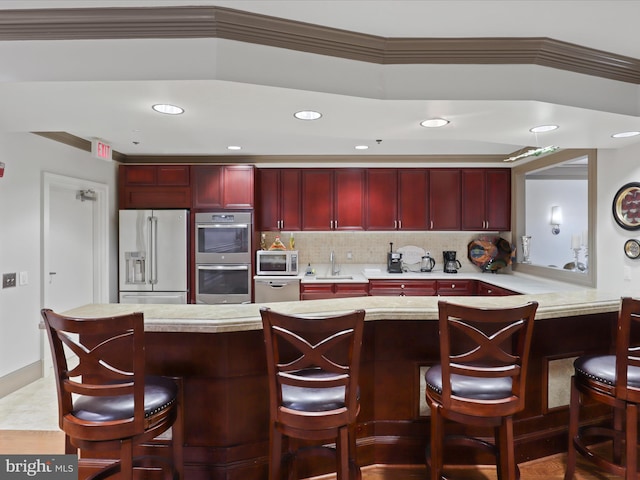 kitchen with sink, stainless steel appliances, a kitchen bar, decorative backsplash, and ornamental molding