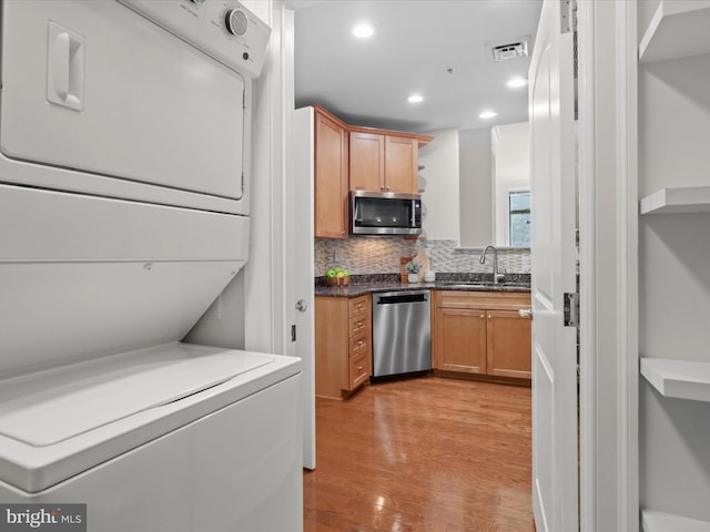 kitchen featuring backsplash, sink, light wood-type flooring, stacked washing maching and dryer, and appliances with stainless steel finishes