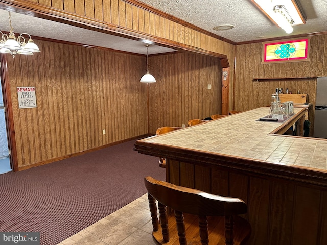 bar with wood walls, tile counters, hanging light fixtures, and ornamental molding