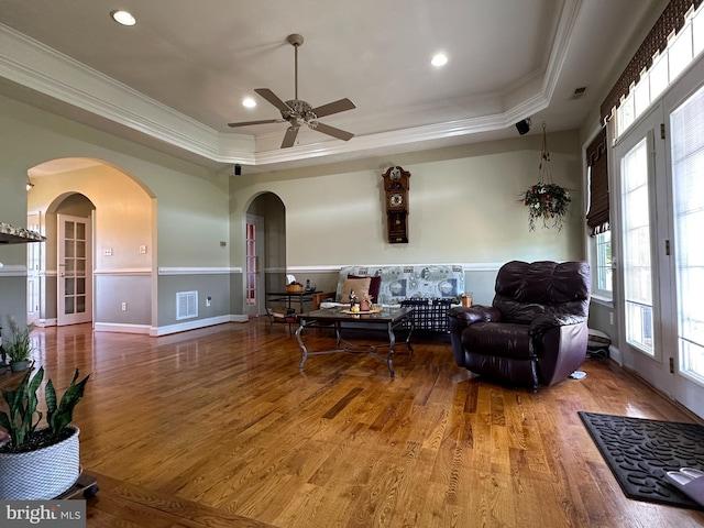 living room featuring ceiling fan, a raised ceiling, ornamental molding, and hardwood / wood-style floors