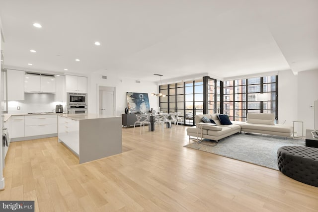 kitchen featuring decorative backsplash, stainless steel appliances, an inviting chandelier, light wood-type flooring, and white cabinets