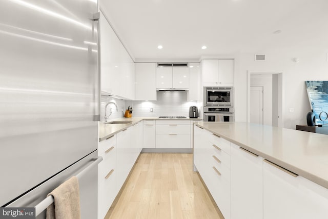 kitchen featuring sink, light wood-type flooring, backsplash, white cabinetry, and stainless steel refrigerator