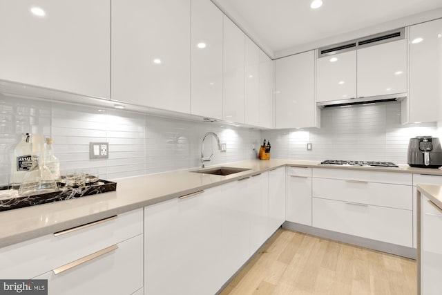 kitchen with white cabinets, sink, light wood-type flooring, backsplash, and stainless steel gas stovetop