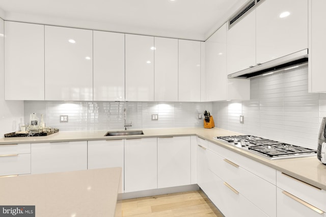 kitchen featuring backsplash, sink, light wood-type flooring, stainless steel gas stovetop, and white cabinetry