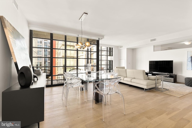 dining area featuring a notable chandelier, light hardwood / wood-style flooring, plenty of natural light, and a wall of windows