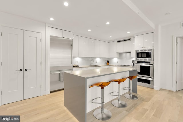 kitchen featuring sink, white cabinetry, light hardwood / wood-style floors, built in appliances, and a breakfast bar