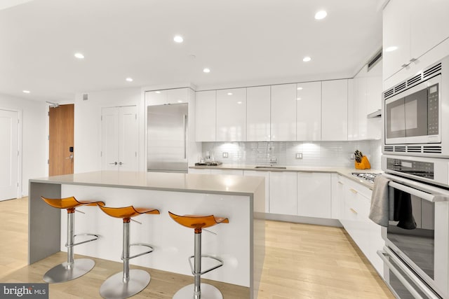 kitchen featuring a breakfast bar area, built in appliances, light wood-type flooring, and white cabinetry