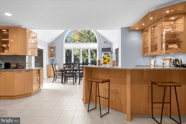 kitchen featuring lofted ceiling, a breakfast bar, light stone countertops, and backsplash