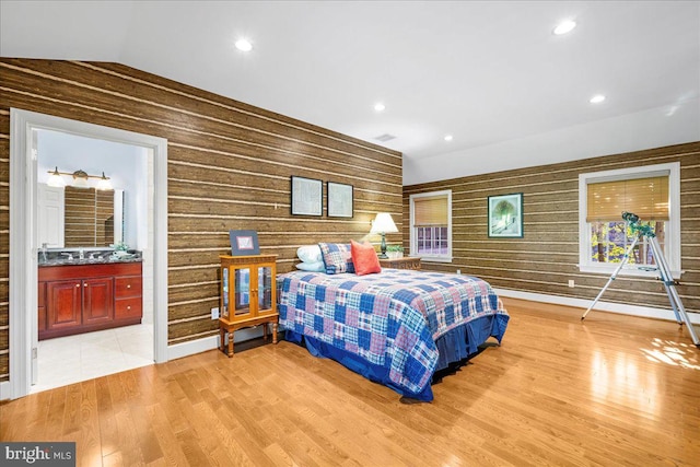 bedroom with ensuite bath, wooden walls, light wood-type flooring, and vaulted ceiling