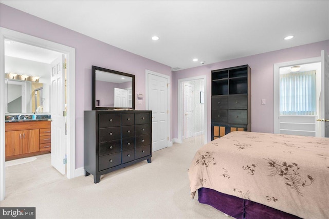 bedroom with sink, light colored carpet, and ensuite bath