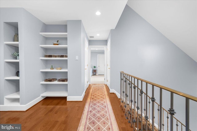 corridor with wood-type flooring and built in shelves