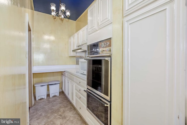 kitchen with light tile patterned flooring, double oven, white cabinetry, pendant lighting, and a notable chandelier