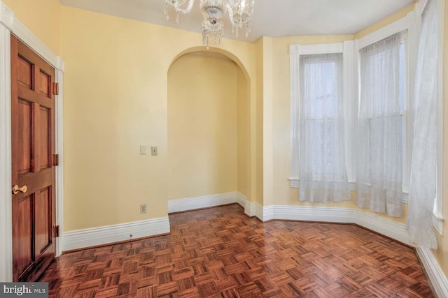 unfurnished room with dark parquet flooring and a chandelier