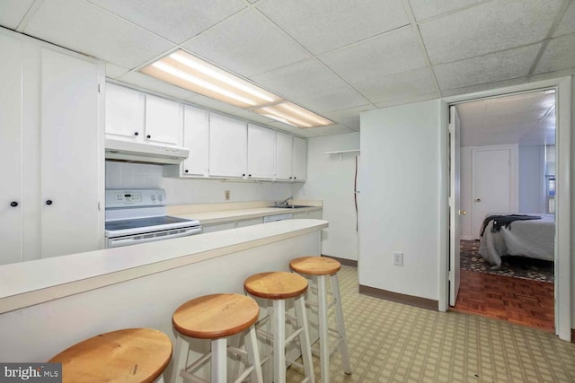 kitchen with decorative backsplash, a breakfast bar area, white electric range, white cabinets, and a paneled ceiling