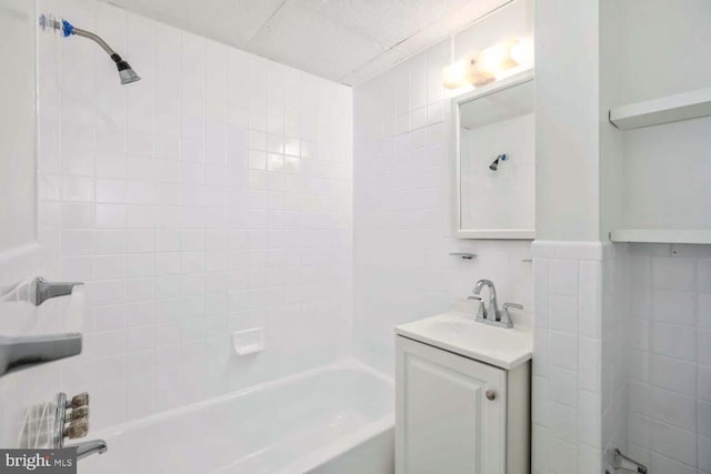 bathroom with vanity, tiled shower / bath combo, and tile walls