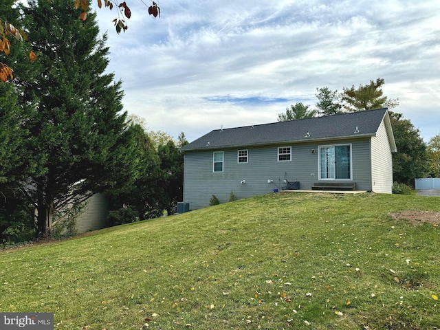 rear view of property featuring central air condition unit and a lawn