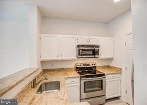 kitchen featuring light stone countertops, stainless steel appliances, white cabinetry, and sink