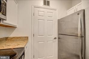 kitchen with stainless steel fridge, light stone counters, and white cabinetry