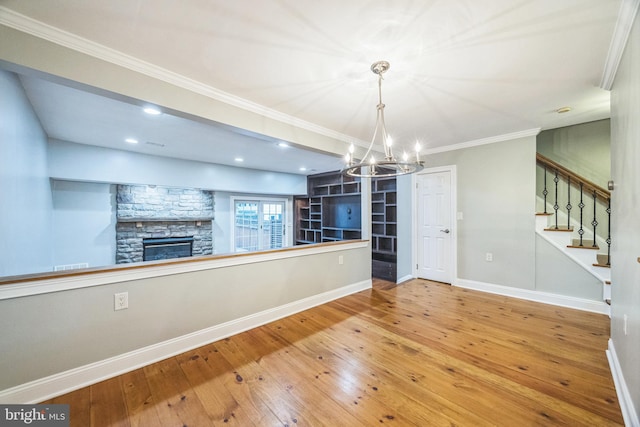 unfurnished dining area featuring hardwood / wood-style flooring, ornamental molding, an inviting chandelier, and a fireplace