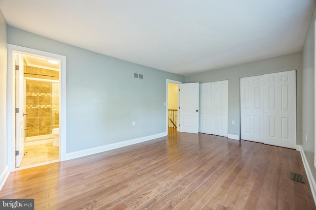 unfurnished bedroom with light hardwood / wood-style floors, two closets, and connected bathroom