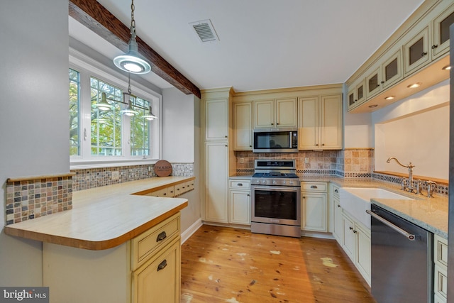 kitchen with kitchen peninsula, hanging light fixtures, light wood-type flooring, sink, and stainless steel appliances