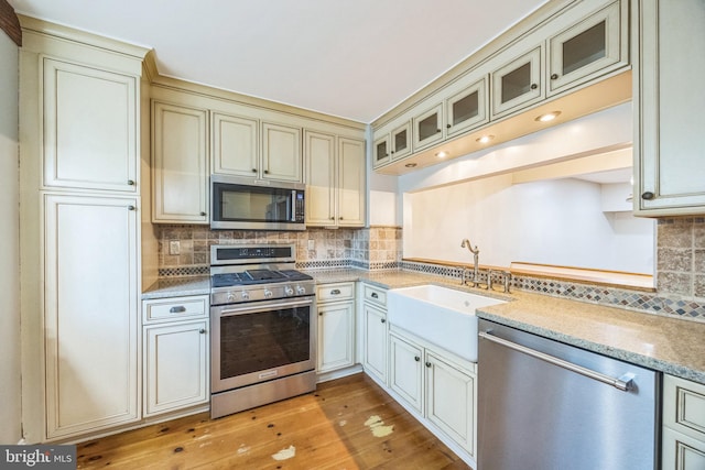 kitchen with cream cabinetry, backsplash, sink, light wood-type flooring, and appliances with stainless steel finishes