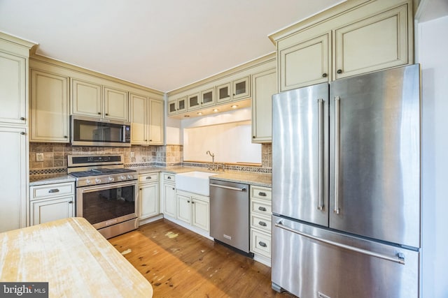 kitchen featuring stainless steel appliances, cream cabinets, sink, and hardwood / wood-style floors