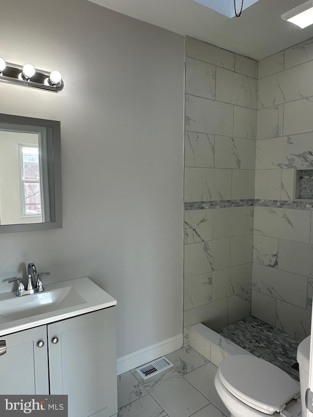 bathroom with toilet, vanity, and a tile shower