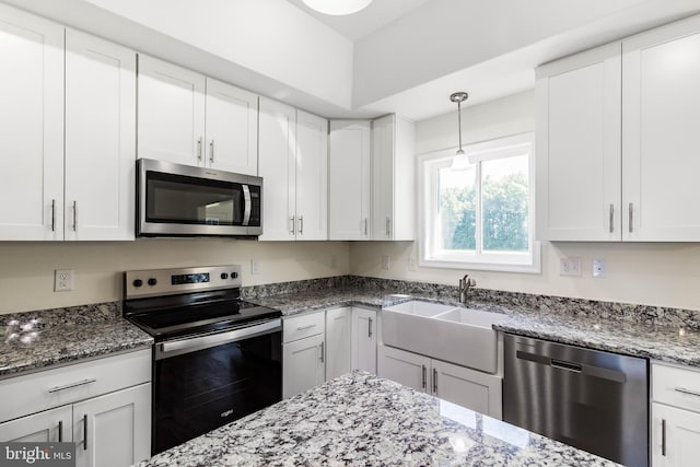 kitchen with dark stone countertops, sink, pendant lighting, white cabinetry, and appliances with stainless steel finishes