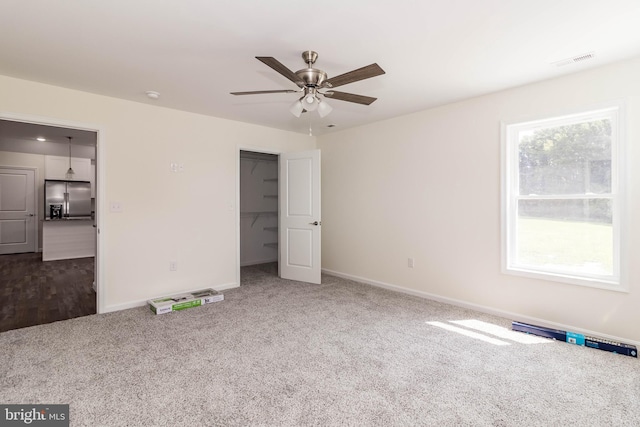 unfurnished bedroom with a spacious closet, stainless steel fridge with ice dispenser, carpet floors, and ceiling fan