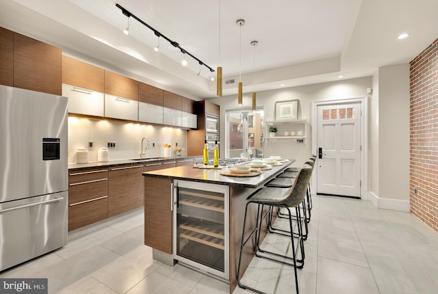 kitchen featuring hanging light fixtures, wine cooler, brick wall, a breakfast bar, and stainless steel refrigerator with ice dispenser