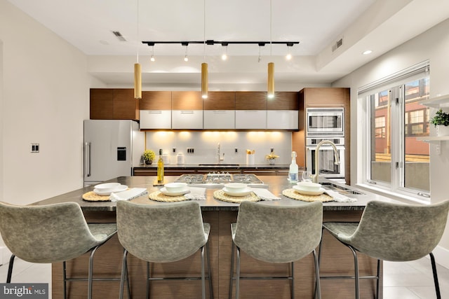 kitchen featuring appliances with stainless steel finishes, light tile patterned flooring, rail lighting, decorative backsplash, and a breakfast bar