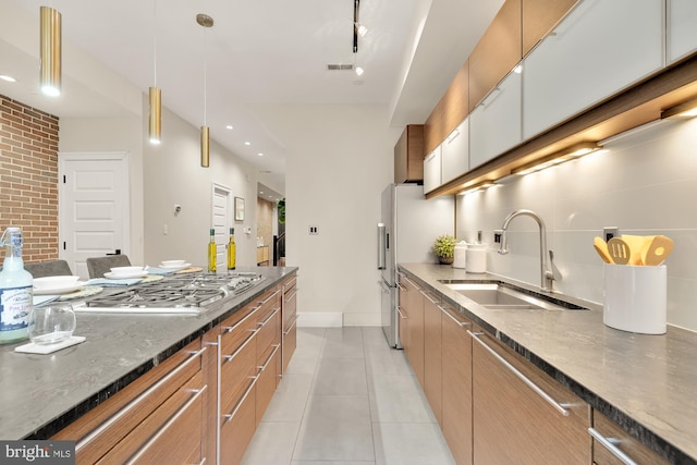 kitchen with light tile patterned floors, dark stone counters, pendant lighting, stainless steel gas cooktop, and sink