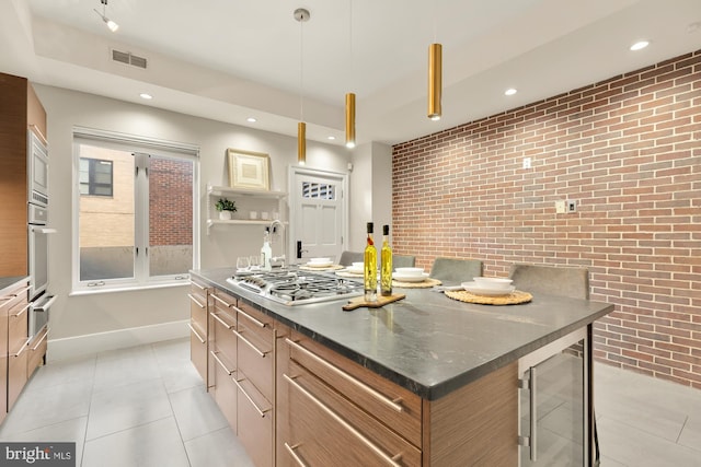 kitchen with appliances with stainless steel finishes, light tile patterned flooring, pendant lighting, a center island, and brick wall