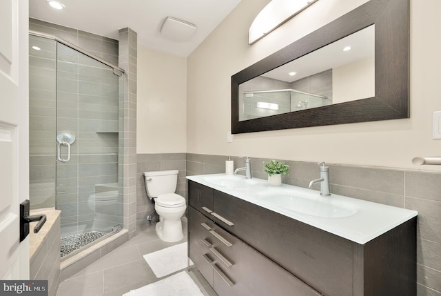 bathroom with toilet, a shower with shower door, vanity, and tile walls