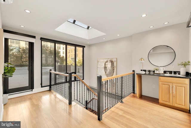 hallway featuring sink, a skylight, and light wood-type flooring