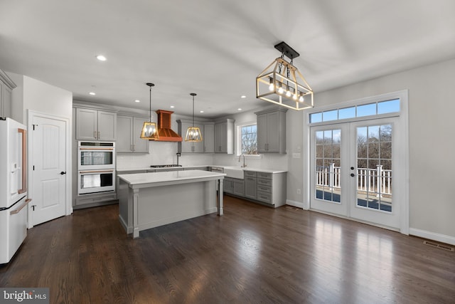 kitchen with hanging light fixtures, a kitchen island, appliances with stainless steel finishes, premium range hood, and gray cabinets