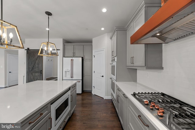 kitchen with hanging light fixtures, a barn door, premium range hood, appliances with stainless steel finishes, and dark hardwood / wood-style flooring