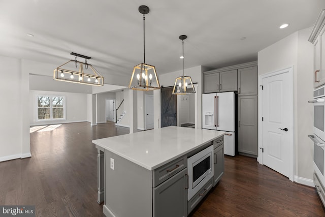 kitchen featuring white fridge with ice dispenser, stainless steel microwave, dark wood-type flooring, gray cabinets, and decorative light fixtures