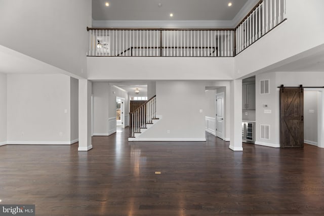 unfurnished living room with a high ceiling, a barn door, and dark hardwood / wood-style flooring