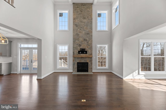 unfurnished living room featuring a stone fireplace, dark hardwood / wood-style flooring, and a high ceiling