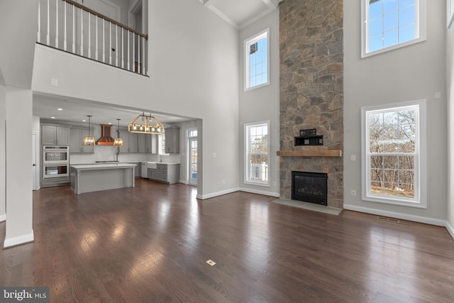 unfurnished living room featuring dark hardwood / wood-style flooring, ornamental molding, a fireplace, a high ceiling, and sink