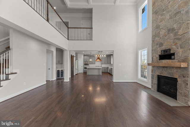 unfurnished living room with ornamental molding, a stone fireplace, a towering ceiling, and dark hardwood / wood-style flooring