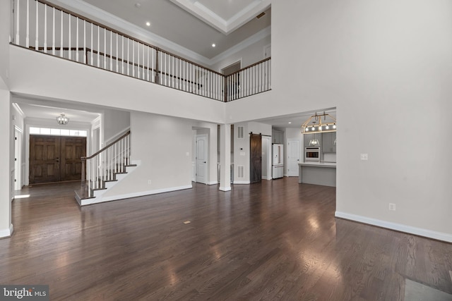 unfurnished living room with a towering ceiling, dark hardwood / wood-style flooring, and a barn door