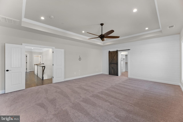 unfurnished bedroom with ornamental molding, a barn door, carpet floors, and a raised ceiling